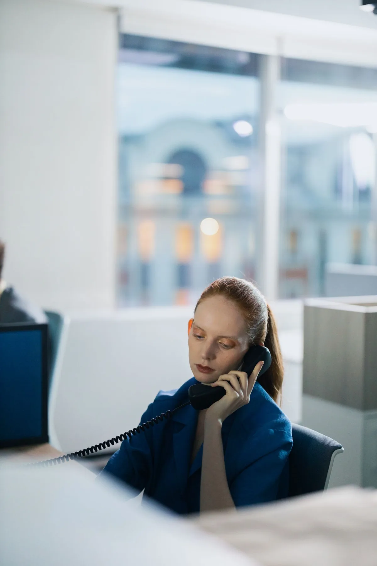 A woman answering a desk phone in a bright office